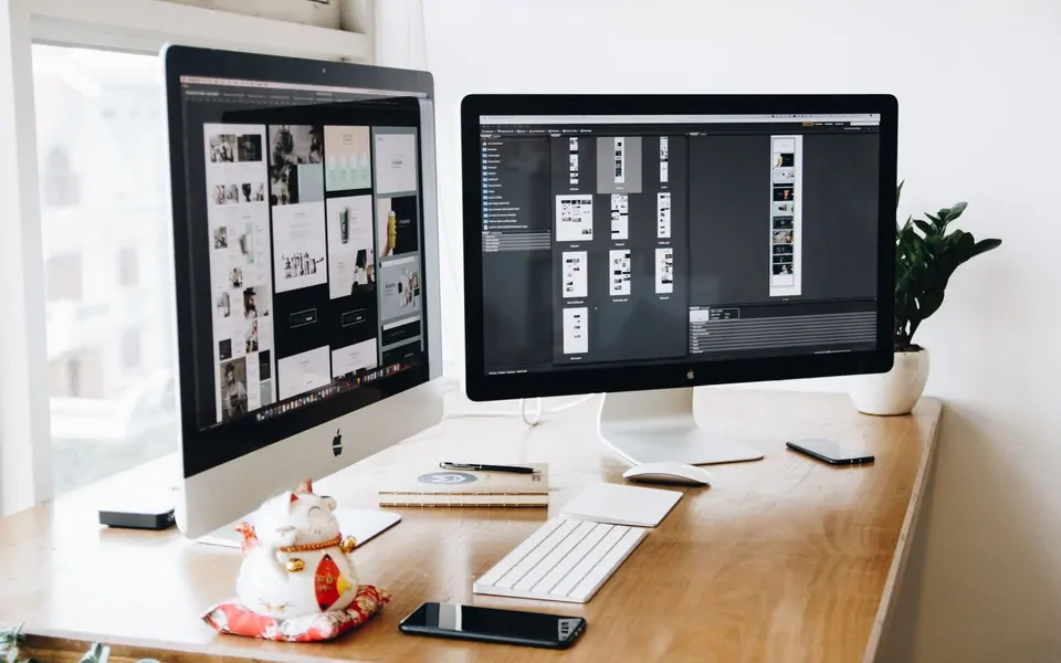 Ahşap masa üzerinde iki monitörde arayüz ve web tasarımı çalışması