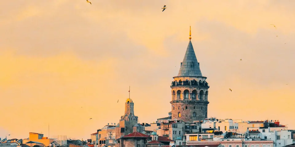 Gün batımında turuncu gökyüzü altında Galata Kulesi ve Beyoğlu çatıları